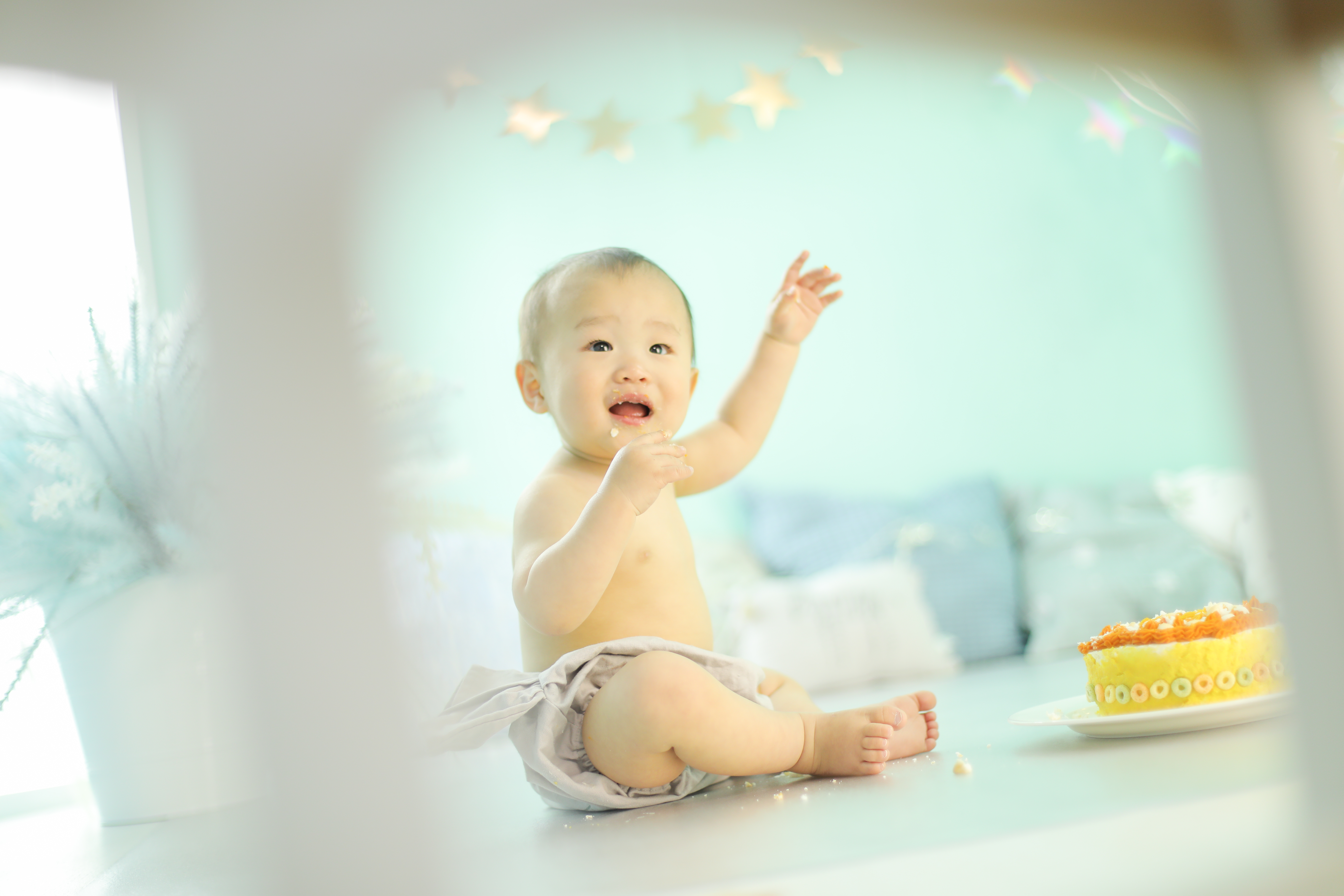 男の子の赤ちゃんがケーキを食べながら手を上げている写真
